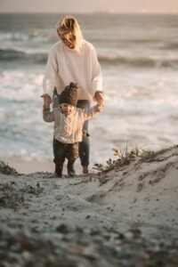 A mother and toddler walk hand in hand on a sandy beach during a serene day.