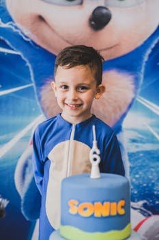 Smiling child in Sonic costume enjoying a themed birthday party with a custom cake.